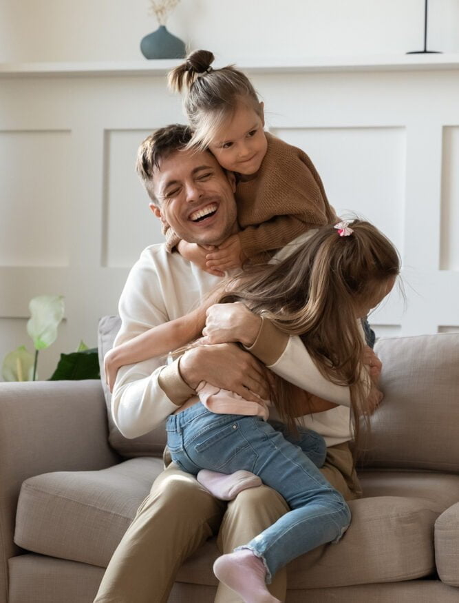 Happy father enjoying time with his children A father smiling and hugging his kids at home, representing the importance of maintaining healthy smiles