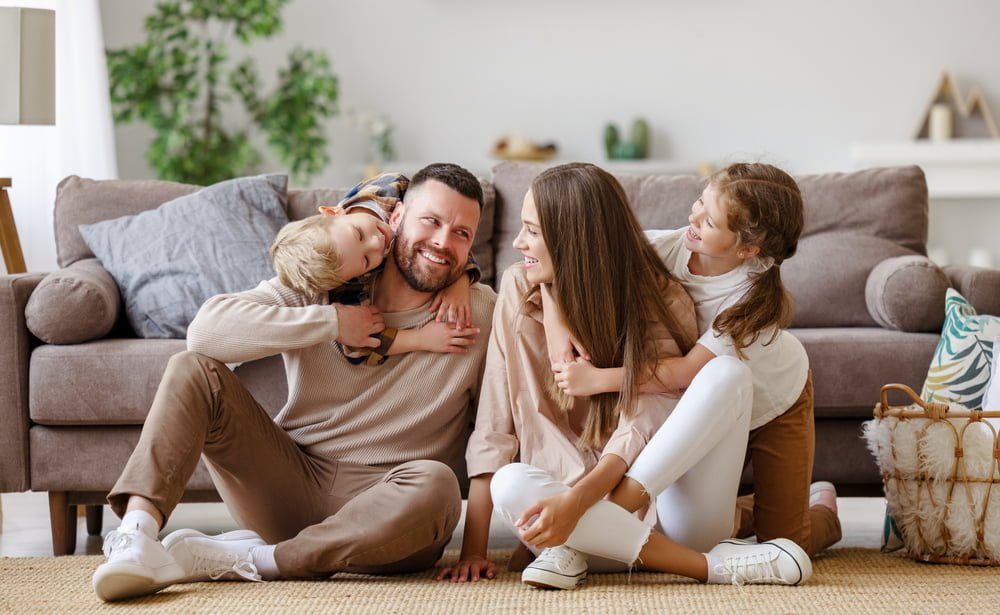 Happy family enjoying quality time together at home  Smiling parents sitting on the floor with their two children hugging and laughing in a cozy living room
