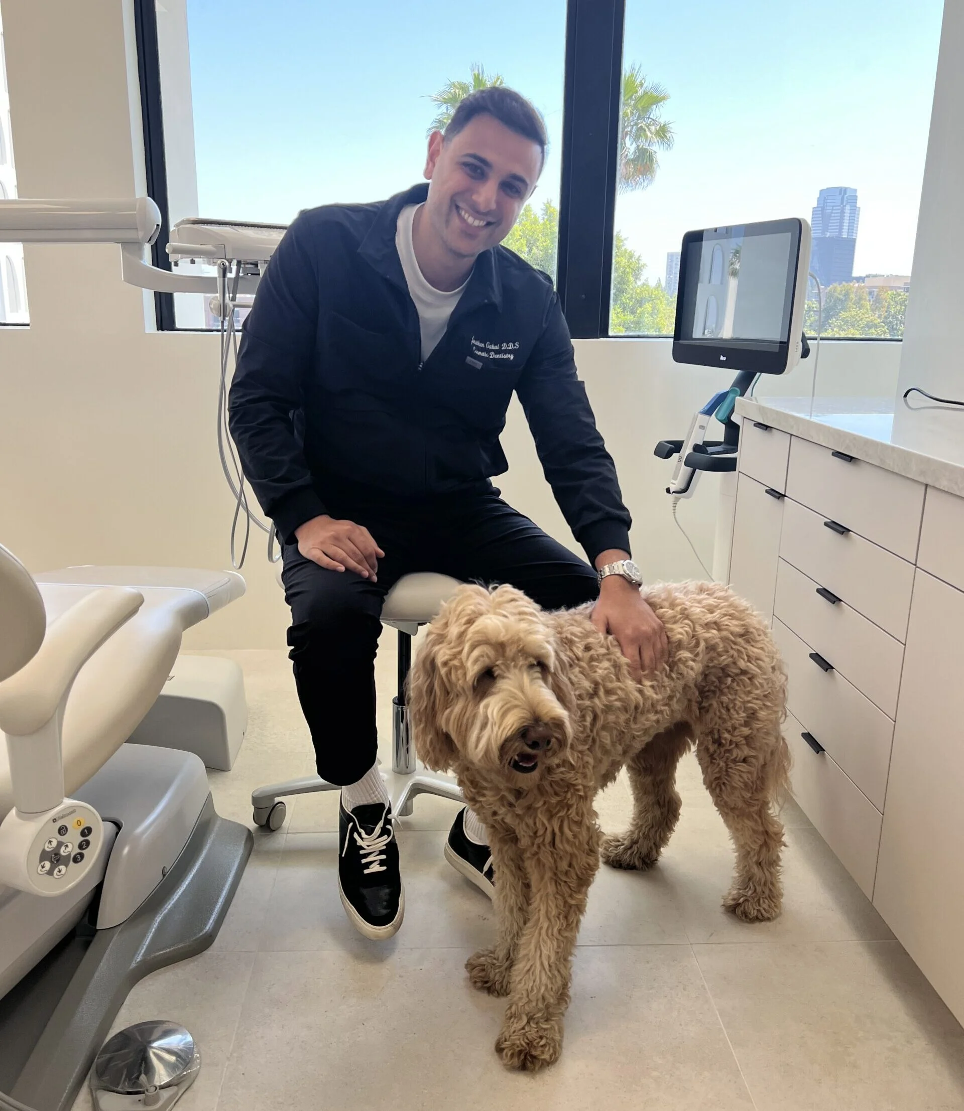 Dr. Jonathan Gabai shares a warm moment with his dog inside a sleek, high-tech dental clinic. A welcoming environment for every patient – Beverly Hills Dentistry.