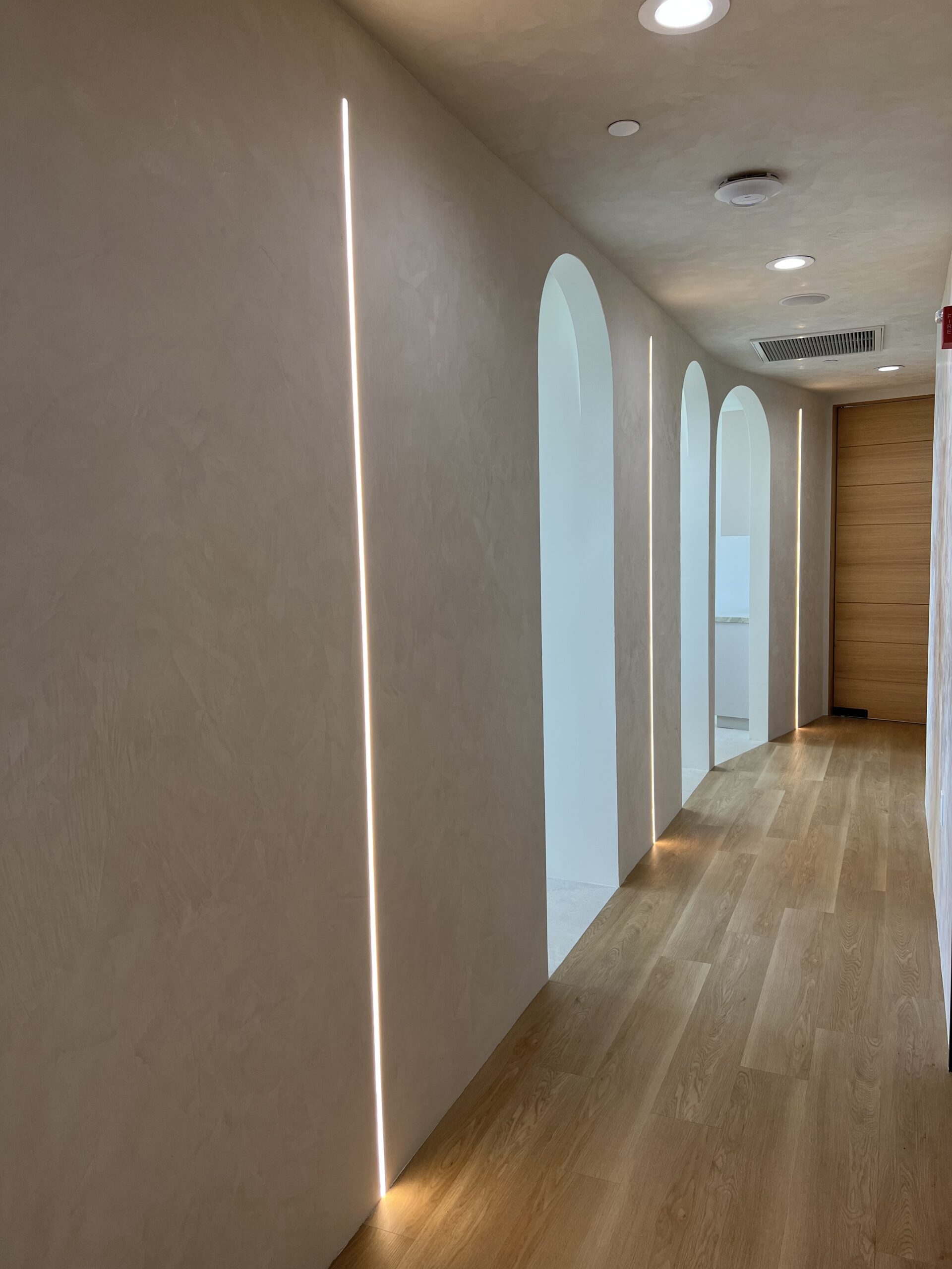 Minimalist hallway featuring wood flooring, ambient vertical lighting, and arched cutouts in a luxury Beverly Hills dental clinic – Invisalign Beverly Hills