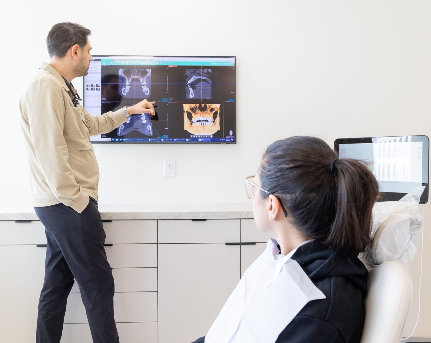 Dentist reviewing dental X-rays with patient – Dental Cleaning in Beverly Hills, CA A dentist points to detailed dental X-rays displayed on a wall-mounted screen while explaining results to a patient seated in the exam chair, highlighting modern technology and patient-focused care – Dental Cleaning in Beverly Hills, CA