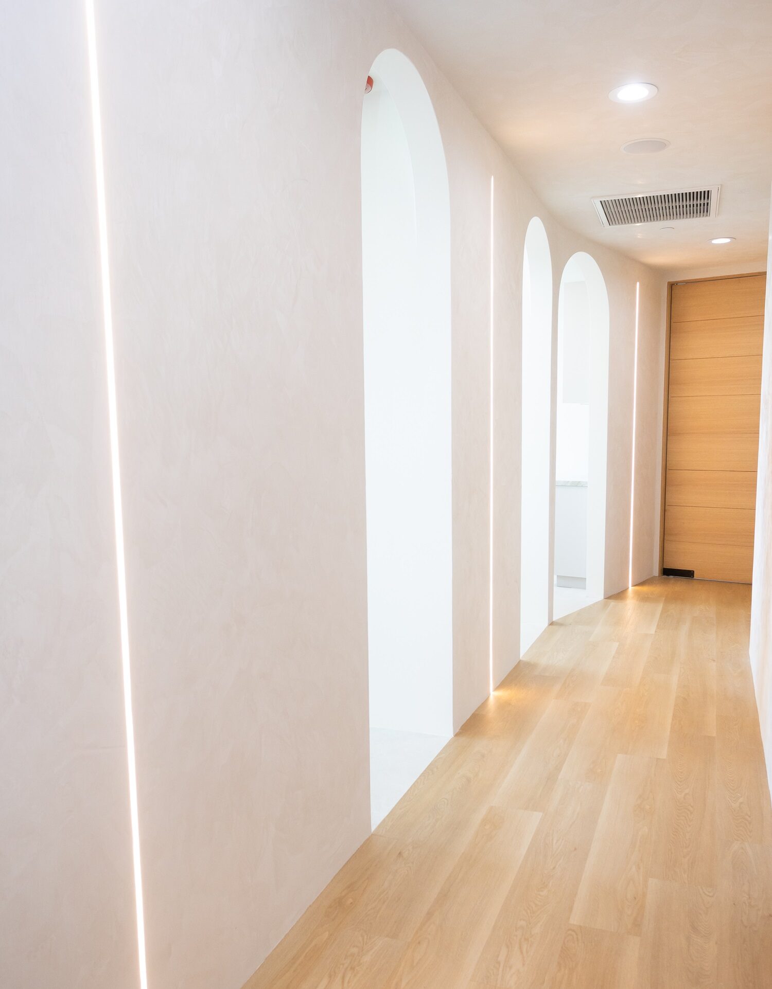 Bright modern hallway with arch design – Dental Cleaning in Beverly Hills, CA A clean, modern dental office hallway with soft lighting, wooden floors, and elegant arched doorways, creating a welcoming and calming atmosphere – Dental Cleaning in Beverly Hills, CA