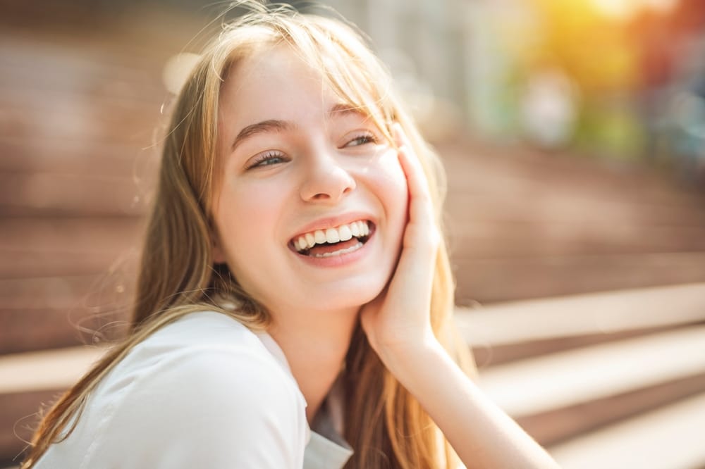 Bright Outdoor Smile After Veneers  Young woman laughing joyfully in the sun, revealing a flawless smile
