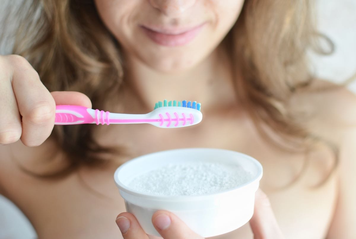 Woman holding a toothbrush over a bowl of baking soda, preparing a natural remedy for teeth whitening at home.