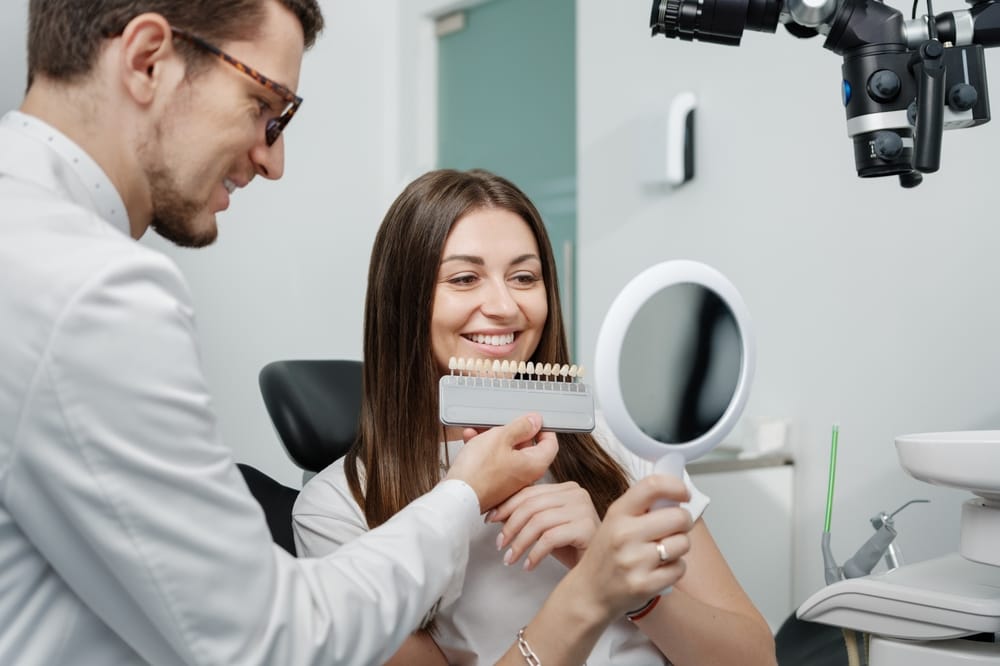 Patient reviewing smile transformation options Smiling woman holding mirror while discussing veneer shades with dentist