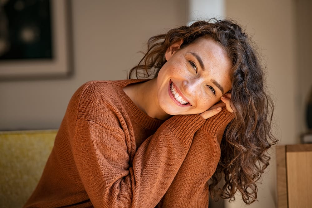 Woman smiling confidently with bright teeth – Veneers Los Angeles Young woman with curly hair smiling brightly after cosmetic dental treatment – Veneers Los Angeles